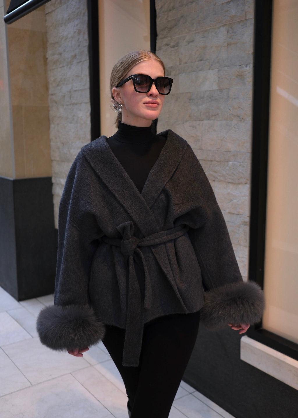 Woman wearing a dark gray coat with fur trim in an indoor setting.