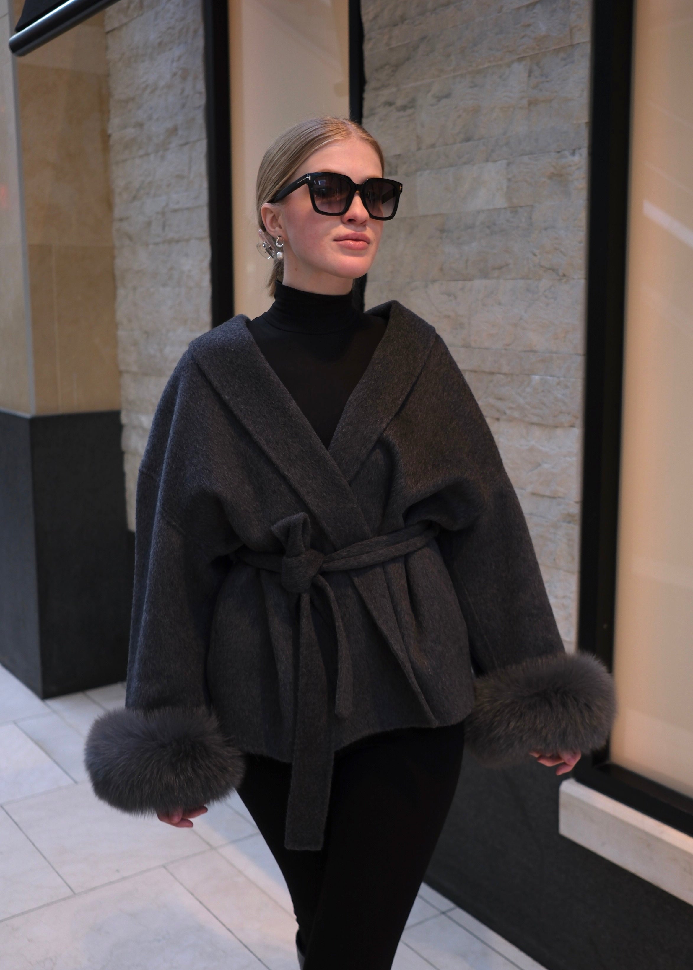 Woman wearing a dark gray coat with fur trim in an indoor setting.