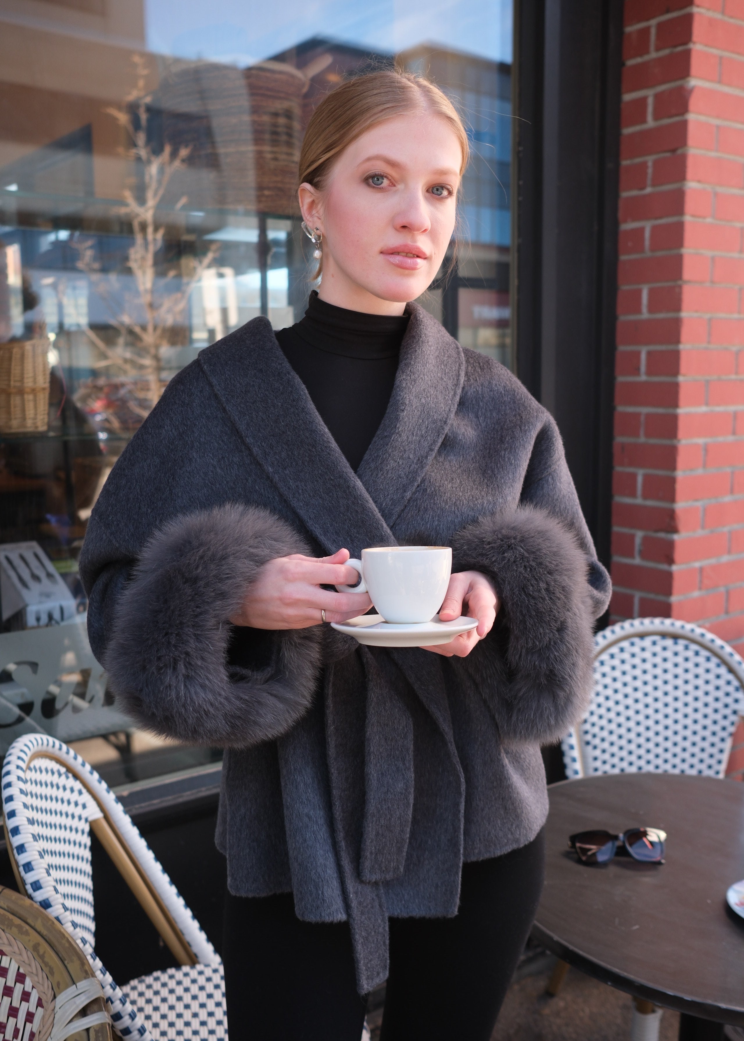 Person wearing a gray coat with fur trim in an urban setting