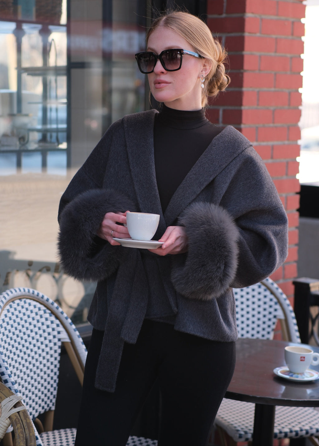 Person wearing a dark coat with fur collar in an urban setting