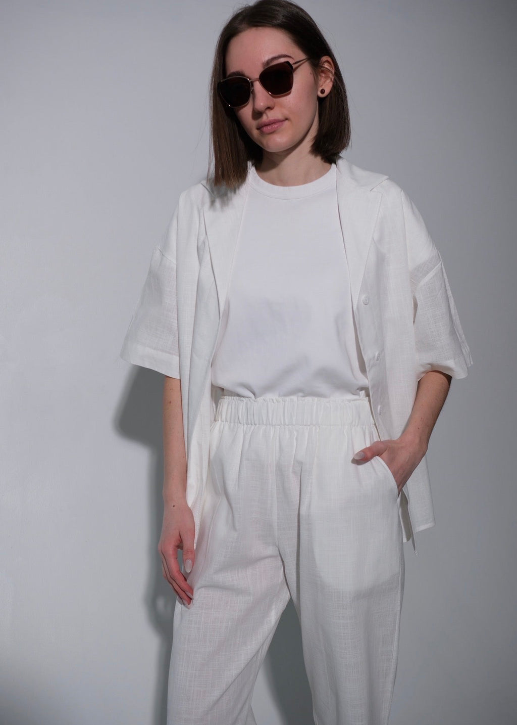Person wearing a white outfit with sunglasses on a plain background