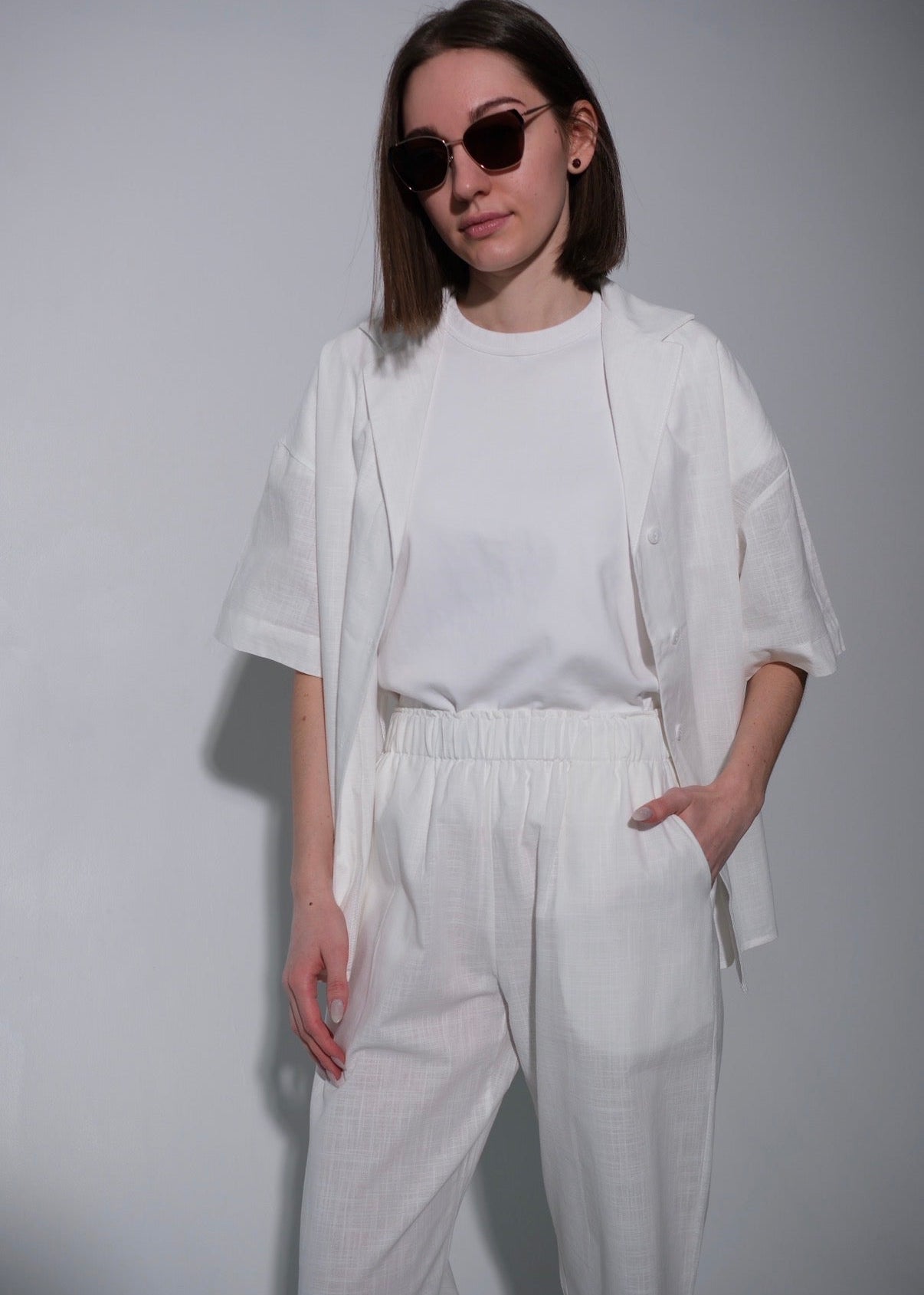 Person wearing a white outfit with sunglasses on a plain background