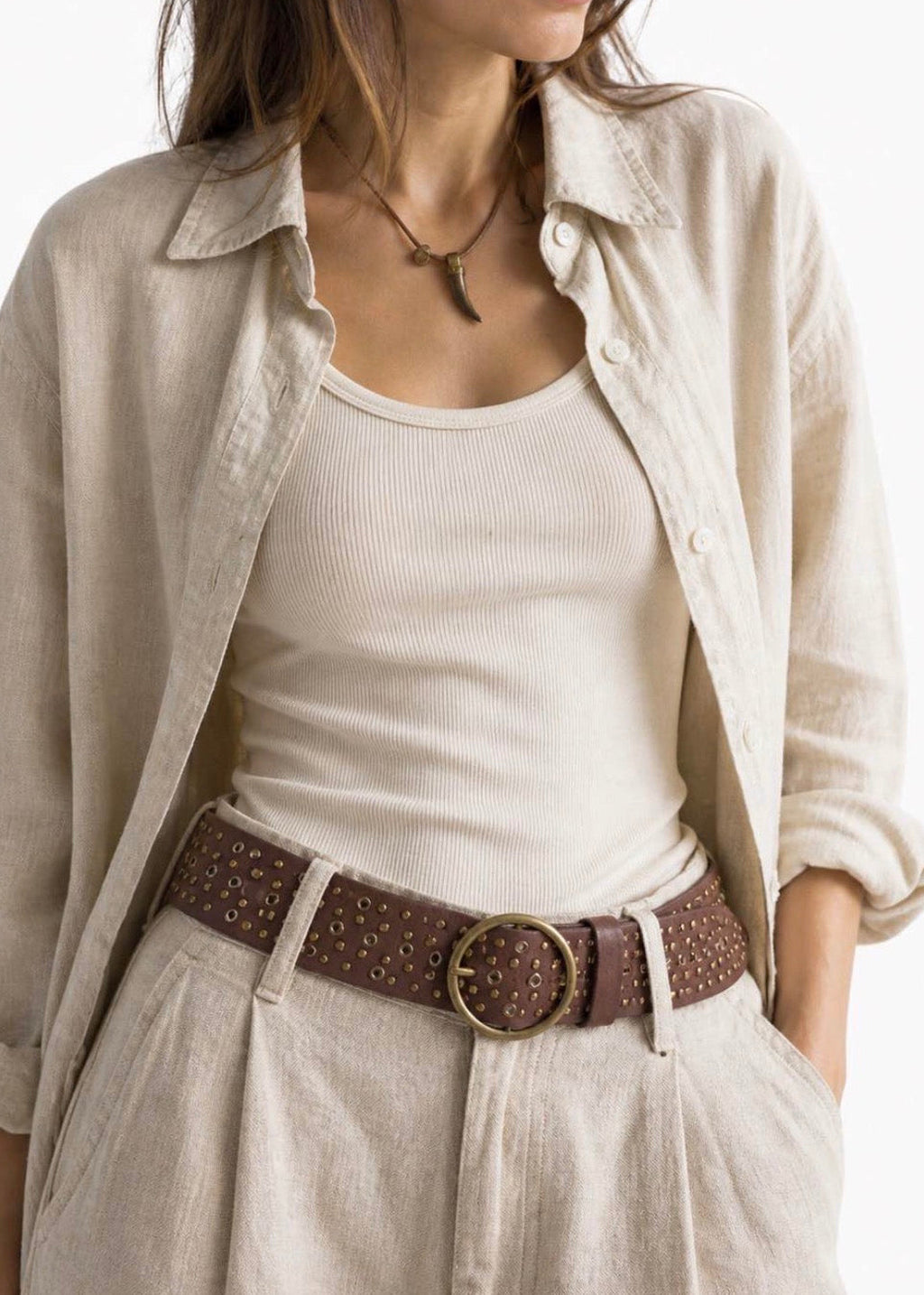 Woman wearing a beige shirt over a white top with a brown belt.