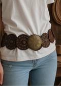 Person wearing a white t-shirt and blue jeans with a decorative brown belt.
