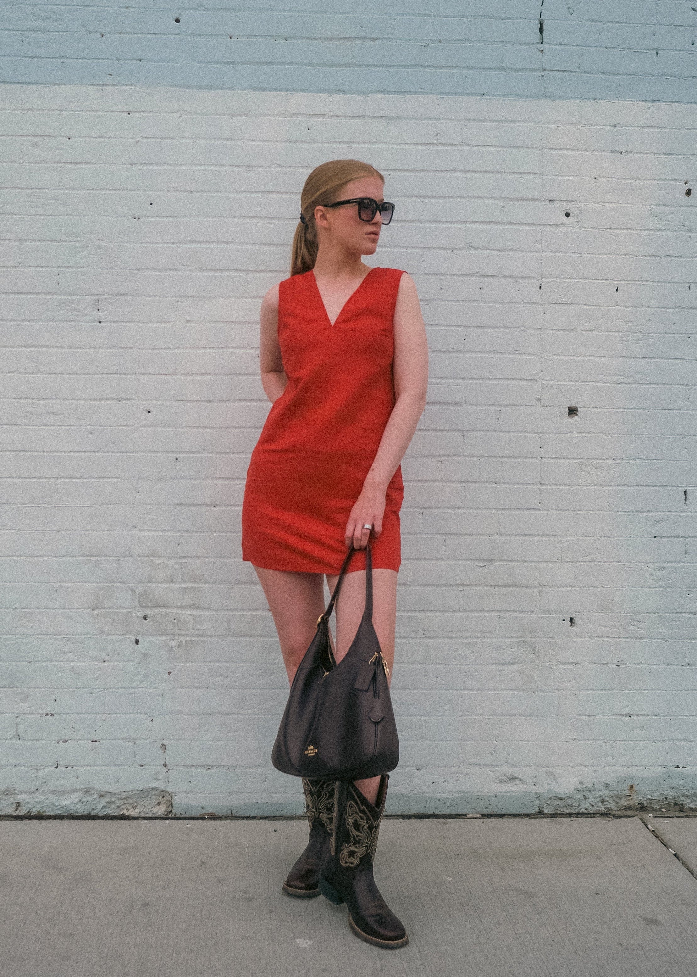 Woman in a red dress standing against a light blue and white brick wall.