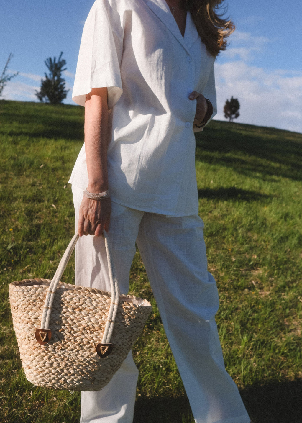 Person in white outfit holding a straw bag in a grassy field