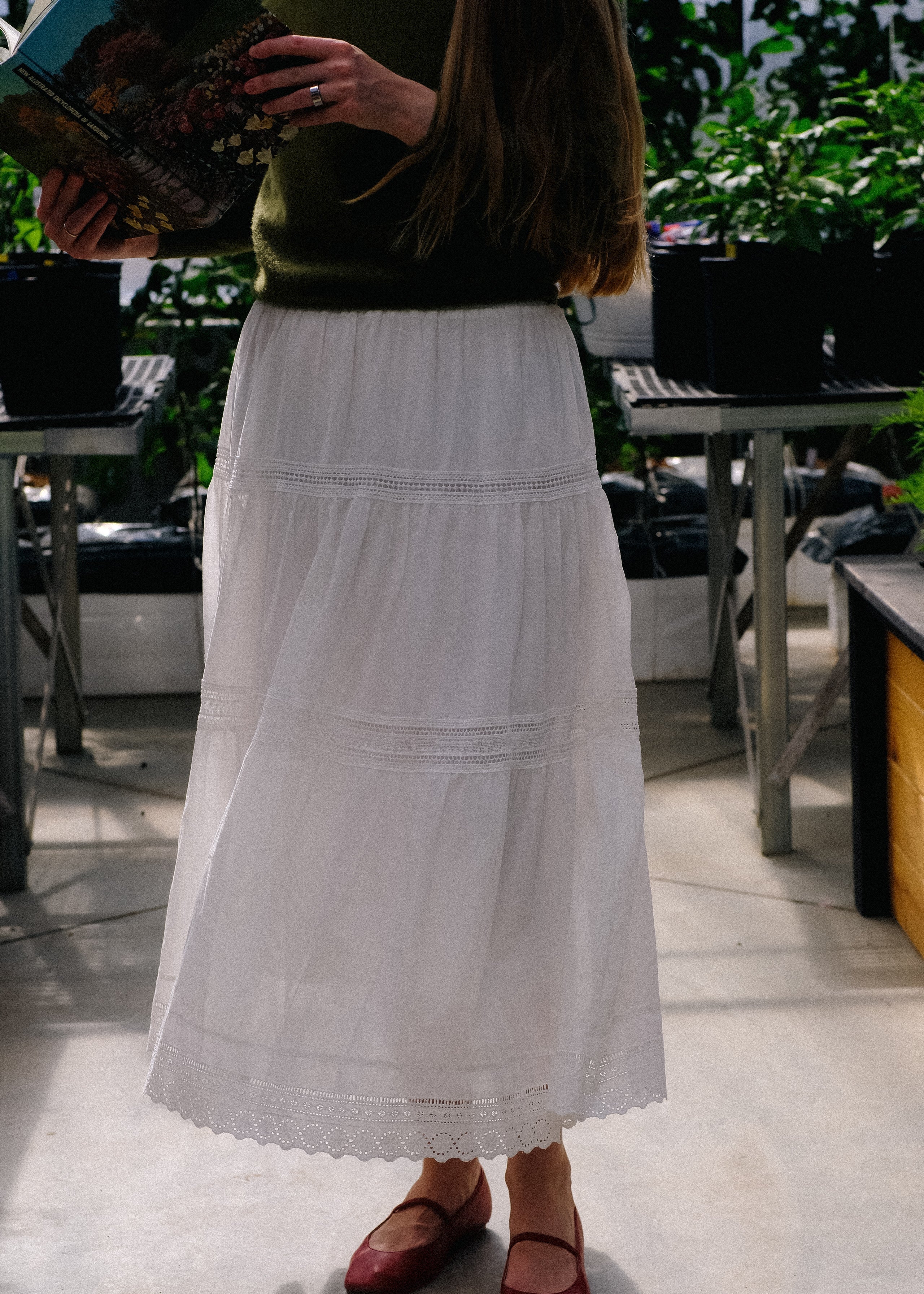 Person wearing a white skirt and red shoes standing outdoors.