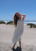 Woman in a white dress standing on a sandy beach with a clear blue sky.