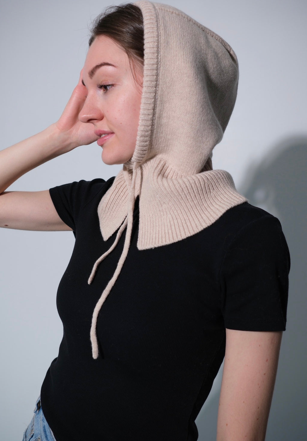 Woman wearing a beige knitted hood over a black top against a plain background
