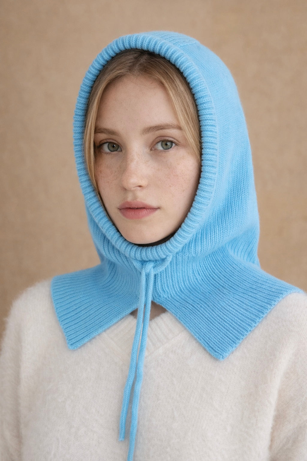 Person wearing a light blue knitted bonnet against a beige background