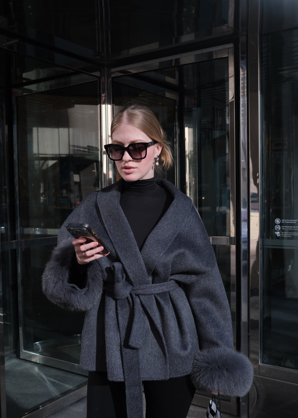 Person wearing a dark coat and sunglasses standing on a reflective surface.