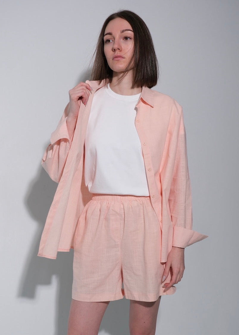 Person wearing a light pink outfit with a jacket and shorts on a plain background