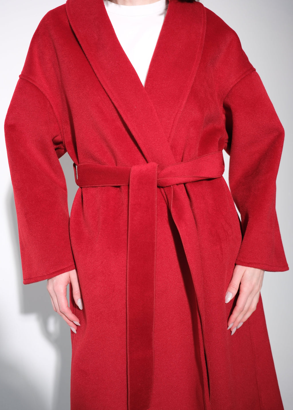 A person wearing a bright red wrap-style coat with a matching tie belt over a white top, photographed against a plain light background.